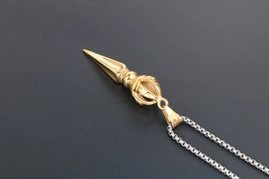 Detailed macro view of a gold-plated Vajra pendant with a silver box chain necklace