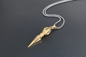 Close-up of golden Vajra pestle pendant with silver chain over grey background