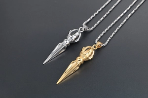 Macro shot of gold and silver Vajra Pestle pendants on box chains over grey texture