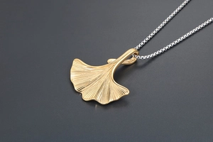 Macro del ciondolo a foglia di ginkgo dorata con texture dettagliata su catena argento