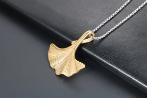 Macro del ciondolo a foglia di ginkgo dorata con venature su una catena a scatola argento