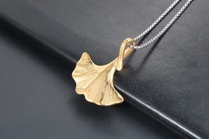 Dettaglio macro del ciondolo a foglia di ginkgo dorata con trama fine su sfondo di pelle