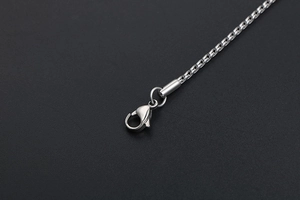 Macro detail of silver Spiga wheat chain necklace with lobster clasp in polished steel