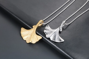 Macro di ciondoli a foglia di ginkgo oro e argento con venature dettagliate su pelle nera