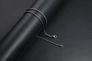 Detail of twisted cable chain necklace with lobster clasp on a dark cylindrical stand