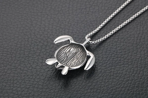 Detailed close-up of a silver turtle pendant with realistic shell textures on a black surface