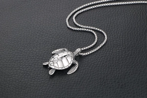 Detailed view of a silver turtle pendant on a black leather texture background