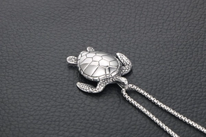 Detail of a polished sea turtle pendant on a black leather surface with a box chain