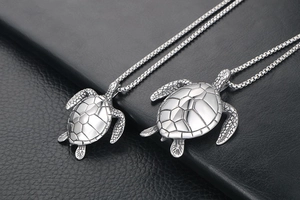 Detailed close-up of two different sizes of titanium steel sea turtle pendant necklaces