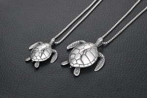 Detailed macro view of two silver turtle pendants with hexagonal shell texture and box chains