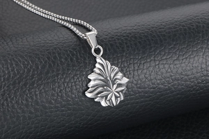 Gros plan du pendentif feuille d'érable argentée avec texture sur cuir noir