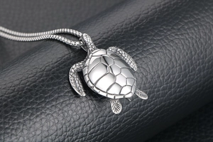 Macro detail of silver sea turtle pendant with geometric back on black leather