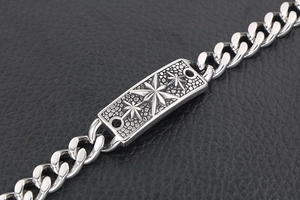 Détail d'un bracelet gourmette argenté avec un charme rectangulaire gaufré d'étoile