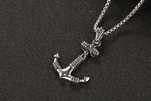 Macro shot of silver anchor pendant with rope details on a black textured surface