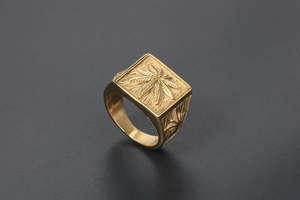 Detailed view of a gold square signet ring with engraved leaf pattern and relief texture