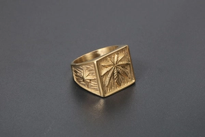 Macro view of gold signet ring featuring engraved leaf motif and textured vintage details