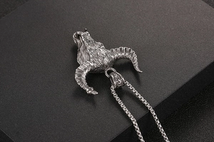 Close-up of a silver ram head pendant with textured horns on a black surface