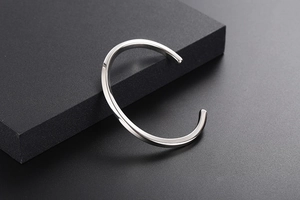 Minimalist silver twist open cuff bracelet on a matte black geometric display stand
