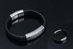 Detail of men's black braided leather bracelet with wheat pattern metal plaque and magnetic clasp