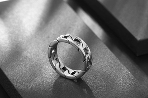 Macro shot of silver Cuban link chain ring on a textured black geometric stand