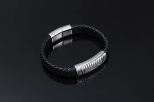 Detail of black braided leather bracelet with silver feather-patterned magnetic clasp