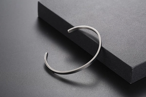 Detailed close-up of a silver matte finish C-shaped cuff bangle on a dark textured display