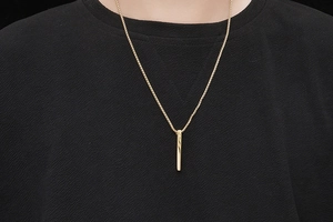 Detailed view of a gold square bar pendant on a box chain worn by a model over black fabric