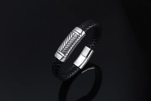 Macro detail of men's braided leather bracelet featuring engraved wheat pattern metal plate
