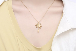 Detail view of a golden palm tree pendant necklace worn on a neck for styling