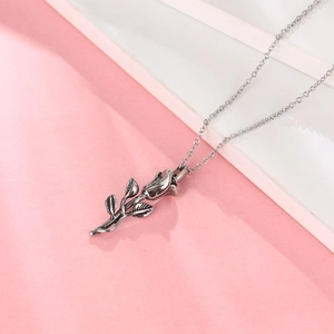 Collier avec pendentif rose en argent vintage et pétales sur une surface rose