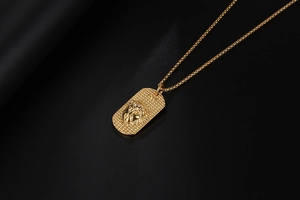 Primer plano detallado del colgante rectangular dorado con relieve de cabeza de león