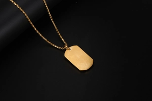 Gros plan d'un pendentif rectangulaire doré sur une chaîne à billes sur fond sombre