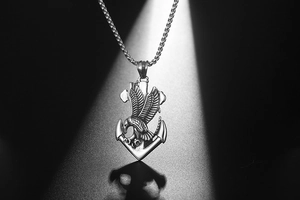 Macro view of eagle and anchor pendant with polished box chain on dark textured surface