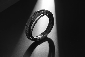 Macro detail of multi-layer black braided leather bracelet with matte metal magnetic clasp