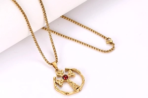 Dettaglio della collana a croce celtica dorata con gemma rossa e catena a scatola