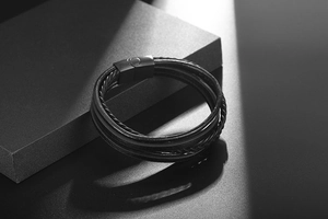 Detail of multi-layer woven leather bracelet with black magnetic clasp and omega symbol