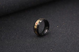 Détail macro d'une bague noire mate avec bande dorée et symboles de cartes de poker