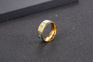 Dettaglio macro dell'anello in titanio dorato con incisioni di rune nordiche blu su grigio
