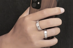 Close-up of polished silver couple rings with hollow cross patterns on a person's hand