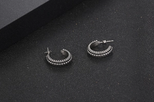 Close-up of silver C-shaped titanium earrings with beaded texture on a black surface