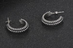 Detail view of silver C-shaped hoop earrings with textured beaded pattern and retro finish