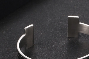 Macro shot of silver metal open cuff bracelet featuring T-shaped ends and engraved runes