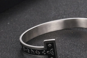 Macro detail of Nordic Viking runes and hammer motif on brushed silver cuff bracelet