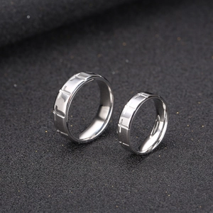 Polished titanium steel couple rings with embossed cross pattern on textured background