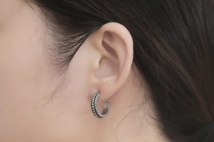 Detail view of retro C-shaped steel earrings with double row bead texture on ear lobe