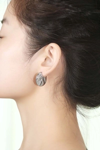 Macro side view of silver liquid metal style irregular hoop earring worn by a model
