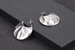 Macro detail of silver fan-shaped irregular textured earrings on black display box