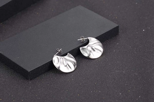 Macro shot of silver hammer-textured C-shaped earrings on a matte black display stand
