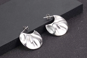 Macro detail of silver fan-shaped earrings with hammered metal texture and butterfly backs