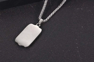 Close-up of a silver stainless steel dog tag pendant with a refined wheat chain necklace